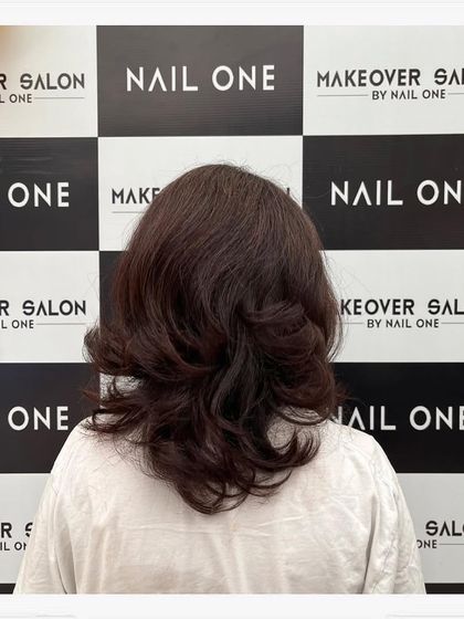 A client showcasing her new layered haircut and color in front of our salon's branding wall. The style has soft waves and beautiful movement.
