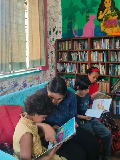 A quiet moment in our Jungle Book Library, where a volunteer reads to children nestled on a cozy couch. The colorful murals and comfortable seating make it the perfect spot to get lost in a good book.