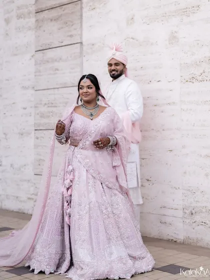 A full-length portrait of the bride in her pastel pink lehenga, looking elegant and poised.