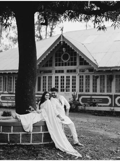 A stunning wide shot in black and white. The couple relaxing under a large tree in front of a heritage building creates a grand and timeless scene.