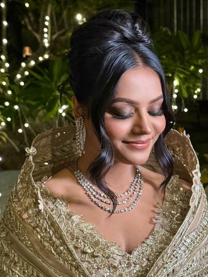 This elegant high bun is styled with soft, wavy tendrils framing the face, creating a glamorous look for a reception or evening event.