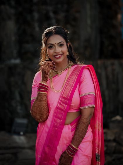 A beautiful outdoor portrait of the bride, Kasturi, in a vibrant pink saree for her engagement. The natural lighting highlights her graceful pose and traditional Maharashtrian look.