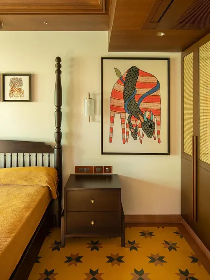 The master bedroom, where a four-poster bed and vibrant yellow floor tiles create a cheerful yet regal atmosphere. A large Gond painting adds a splash of color and story to the wall.