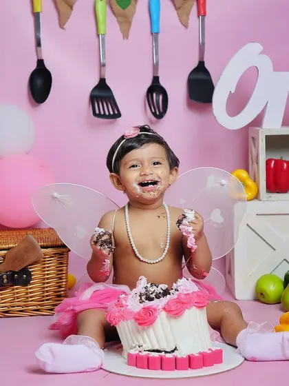 A fairy chef enjoying her first birthday cake. This shot combines a fun theme with the pure joy of a cake smash, complete with fairy wings and a pearl necklace.