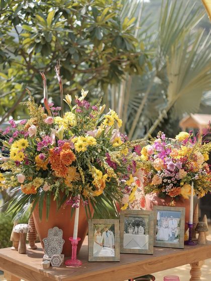 A welcome table at the Rajasthani Haldi, styled with vibrant floral arrangements in terracotta pots and framed photos of the couple, setting a warm and personal tone for the celebration.