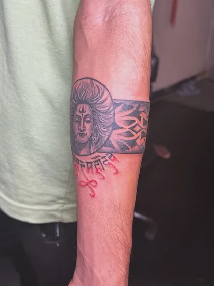 A powerful armband tattoo featuring Lord Shiva's face and the 'Har Har Mahadev' chant in red. This design is a bold declaration of faith that wraps around the arm.