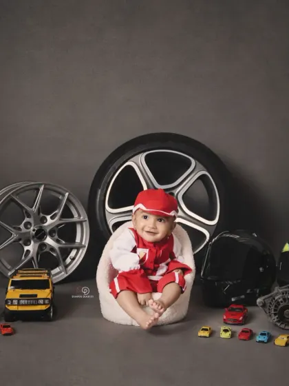 A full view of the 'Biker Baby' setup, featuring a baby boy in a red racing suit surrounded by real car parts, wheels, and toy cars. This is a great example of a highly customized themed session.