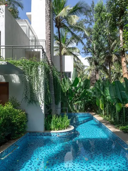 At the SANCTUM House, the swimming pool is designed as a natural element that meanders alongside the home, flanked by the lush greenery of an existing coconut grove. This design choice creates a resort-like feel and reinforces the home's connection to its landscape.