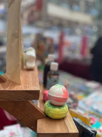 A close-up shot of my bath bombs stacked on the display shelf. The blurred background shows the busy atmosphere of the market, but these little balls of joy always stand out.