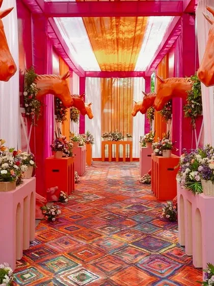 Haldi, but make it equestrian chic. This bold entranceway combines vibrant pinks and oranges with floral-adorned horse sculptures to create a whimsical and unforgettable welcome for a fun-filled celebration.