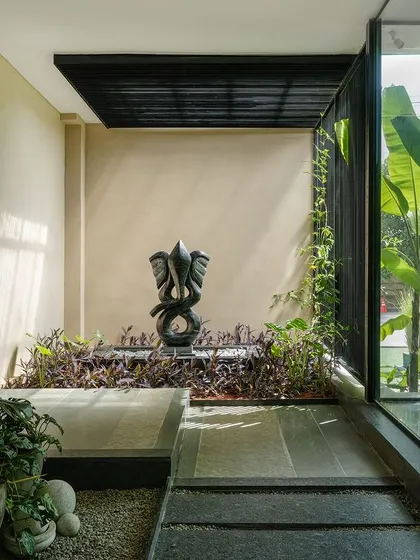 The entrance pathway to the Soul Spring center is designed as a sensory journey. Lush plants and a Ganesha sculpture are meticulously placed to create a feeling of peace and intrigue, setting a contemplative tone upon arrival.