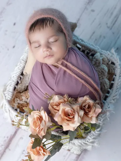 A sweet sleeping baby boy in a mauve wrap and bonnet, nestled in a white basket.