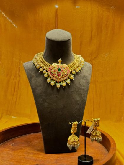 A classic temple jewelry set. The gold choker with its pink and green stone pendant is paired with matching jhumkas for a complete traditional look.