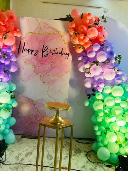 A contemporary backdrop design using a marble-print panel and a unique rainbow-colored balloon arrangement on either side.