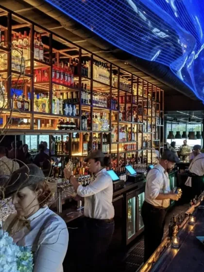 The bustling bar at LokalJC. The design features a dramatic, multi-tiered shelving unit that serves as both storage and a stunning visual centerpiece, lit to create a warm and inviting glow.
