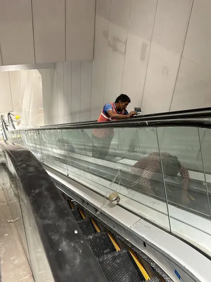 A worker performs final finishing touches on the glass paneling of the escalator. Every detail, no matter how small, is inspected to meet the zero-tolerance standards of a high-end retail environment.