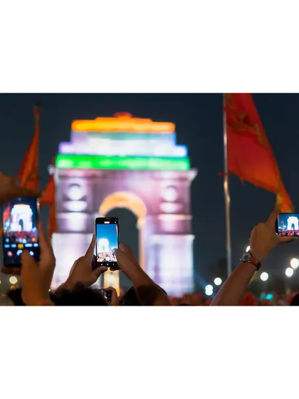 A crowd of people holds up their phones to photograph India Gate, lit up in the tricolor. This image captures a moment of collective patriotism and celebration.