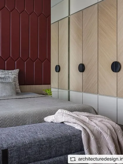 Another view of the bedroom in 'Aria Residence', showcasing the custom wardrobes with a chevron veneer pattern and a bold, geometric red upholstered headboard.