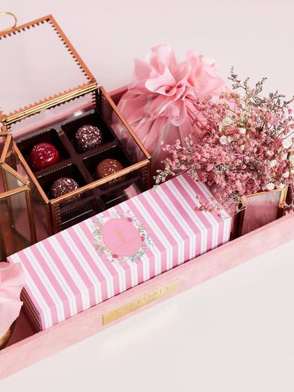An exquisite pink hamper featuring a glass box of bonbons, beautifully packaged treats, and delicate dried flowers.