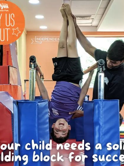 Trying new things from a different perspective. A smiling child hangs upside down on the bars with a coach's support, building confidence and upper body strength.