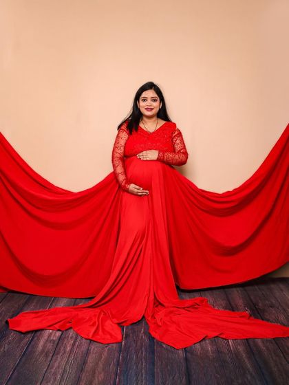 A classic studio portrait focusing on the mother-to-be. The vibrant red lace gown is spread out to create a beautiful, dramatic base, drawing all attention to her and her baby bump.