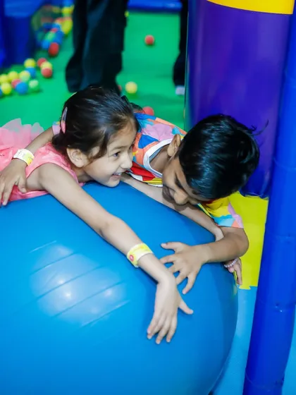 Two toddlers play together on a large yoga ball. This encourages balance, coordination, and cooperative play.