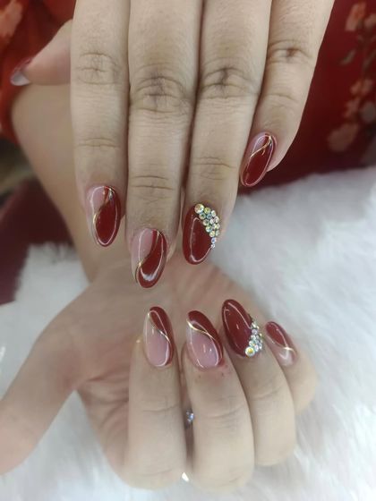 A rich and elegant design combining deep red polish with sparkling rhinestones. The abstract gold lines add a modern touch to this glamorous look.