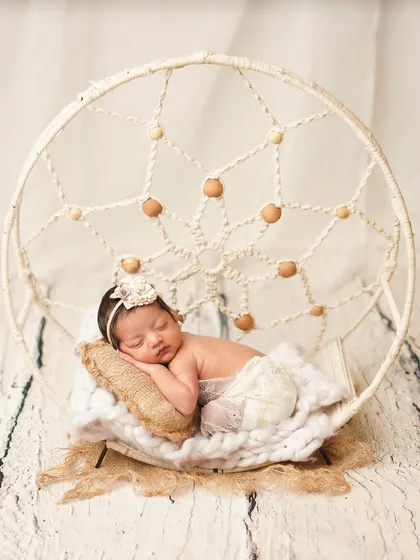 A full shot of the newborn in the dreamcatcher prop. The white, rustic background and natural textures create a serene, bohemian vibe.