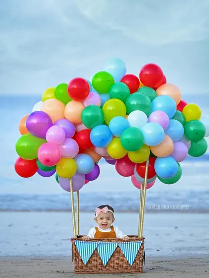 A creative and whimsical baby portrait featuring a little one in a hot-air balloon basket on the beach. This themed shoot uses colorful balloons and a natural seaside setting to create a magical and unforgettable image.