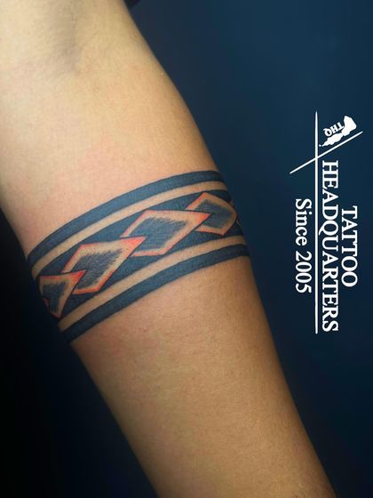 A custom armband tattoo with a chain-link pattern that glows a vibrant red under UV light, a special effect we offer.