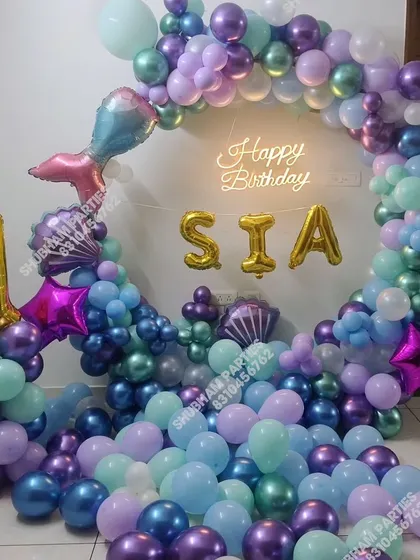An underwater mermaid theme birthday party with a circular balloon garland in shades of purple, blue, and teal.