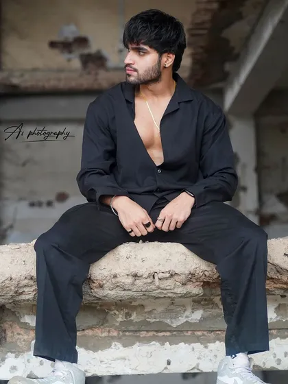 A fashion-forward shot of a model in an all-black outfit. The unbuttoned shirt subtly reveals a defined chest, blending fitness with a cool, edgy style.