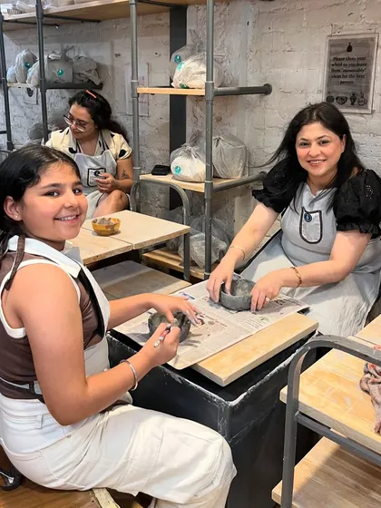A mother and daughter proudly working on their pieces. Our studio is set up to be comfortable and inspiring, with everything you need for a great pottery session.