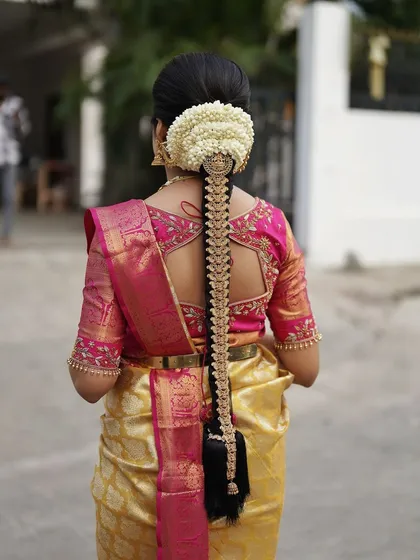 A South Indian bridal look is incomplete without a stunning hairstyle. Here, I've created a traditional long braid, intricately decorated with fresh jasmine flowers and a beautiful golden jadai, perfectly complementing her silk saree.