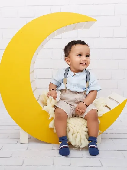 A happy one-year-old boy sits on a bright yellow crescent moon prop for his milestone photoshoot.