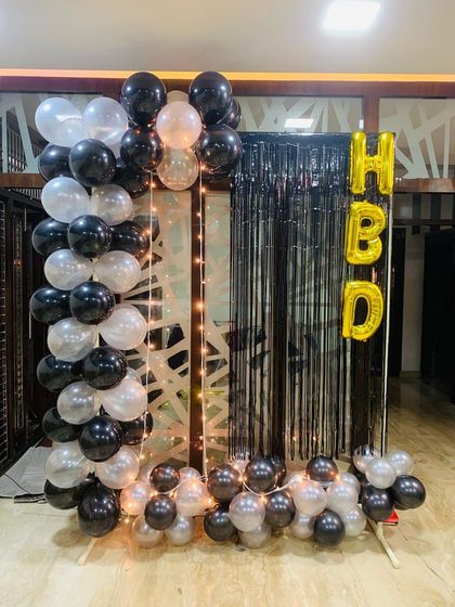 A simple yet striking birthday decoration. I used black and white balloons to create a partial arch, set against a black fringe curtain with 'HBD' foil letters and a string of fairy lights for a cozy glow.