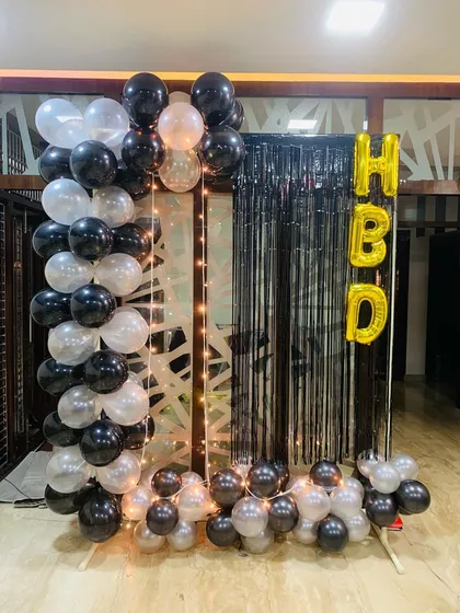 A simple yet striking birthday decoration. I used black and white balloons to create a partial arch, set against a black fringe curtain with 'HBD' foil letters and a string of fairy lights for a cozy glow.