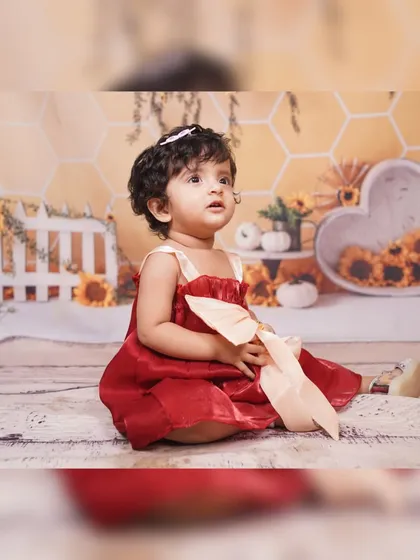 An adorable portrait of the birthday girl in a red dress, which contrasts beautifully with the warm yellow and brown tones of the sunflower-themed set.