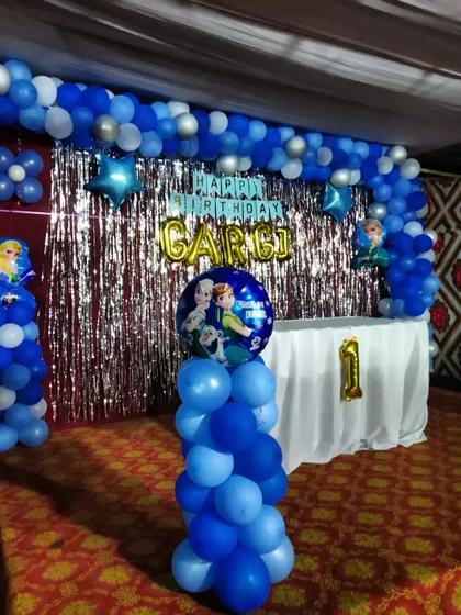A stage decoration for a Frozen themed birthday party. This setup uses shades of blue and silver balloons, a foil curtain backdrop, and character balloons to create a winter wonderland.