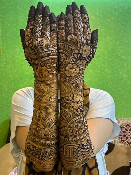 A bride holding her hands up to showcase the back of her full-arm mehndi design, which is just as detailed as the front.