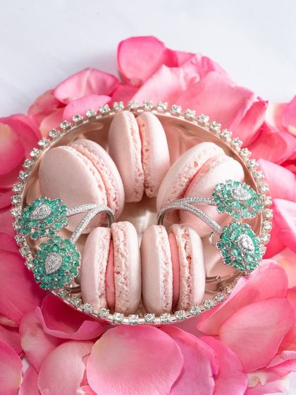 This Valentine's Day, trade the cliché for couture. Here, our stunning emerald and diamond rings are playfully styled with macarons, because she deserves something sweet and something that sparkles.
