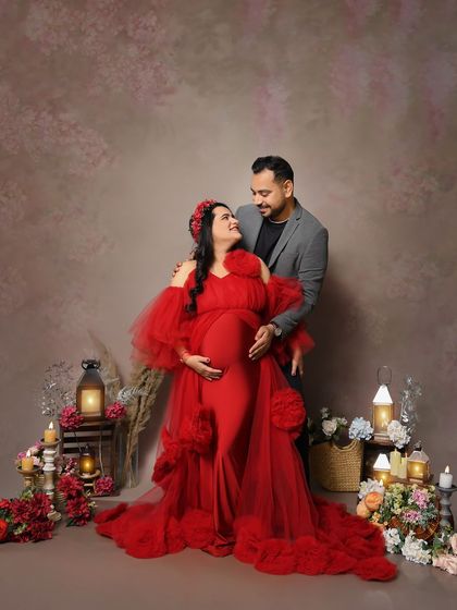 A loving gaze between the couple. The mom-to-be is radiant in a red ruffled gown, surrounded by our rustic prop setup with lanterns and dried flowers.
