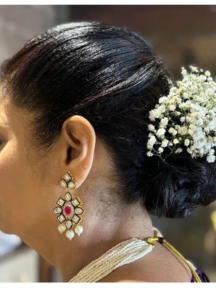 A classic low bun hairstyle, elegantly decorated with a cluster of baby's breath. This is a timeless and sophisticated choice for any formal occasion.