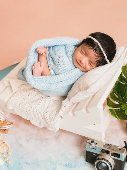 A peaceful newborn sleeps on a miniature beach chair, swaddled and dreaming of the ocean. The details create a complete, imaginative story.