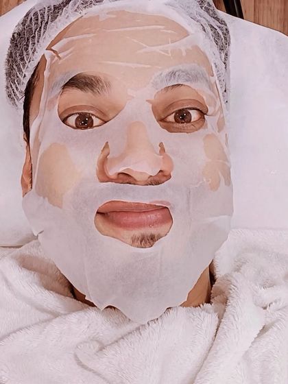 A client relaxing with a sheet mask as part of his facial treatment. This step helps to deeply hydrate and soothe the skin, locking in the benefits of the facial.