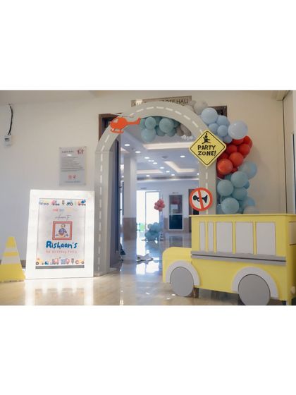 An indoor entrance for a transportation party, with a road arch, a 'Party Zone' sign, and a cute yellow bus prop to welcome the little guests.