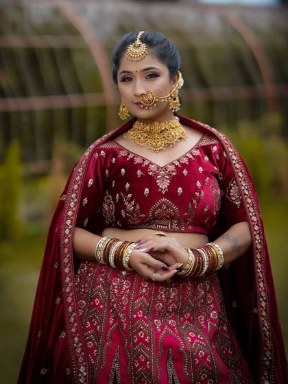 A full-body shot showing the stunning red velvet lehenga. The makeup is balanced to stand out against the rich fabric and detailed embroidery.