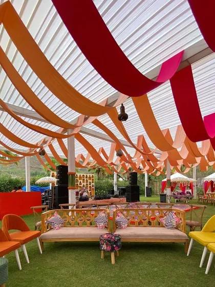 For a vibrant Mehandi, we used a bold color palette of orange and pink. This setup features colorful ceiling drapes and modern, eclectic seating, creating a lively and energetic atmosphere perfect for a party.
