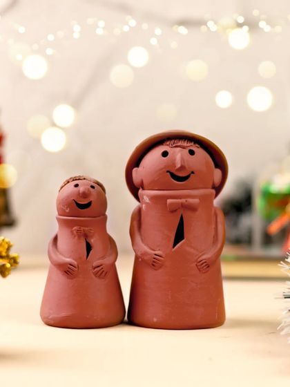 A pair of handmade terracotta figurines, styled to create a joyful and festive scene. This product shot highlights the unique, handcrafted nature of the items.
