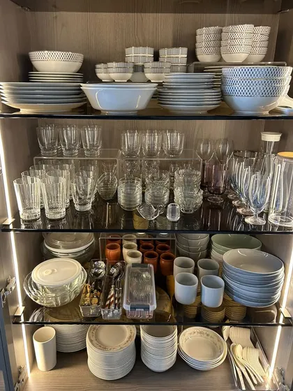 A fully stocked crockery cabinet, organized for a large family or someone who loves to entertain. Every glass, plate, and bowl is grouped by type for easy access.